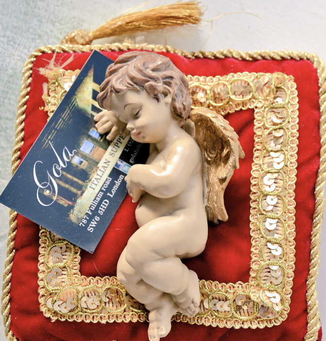 A cherub resting on a red and gold cushion beside a Gola card