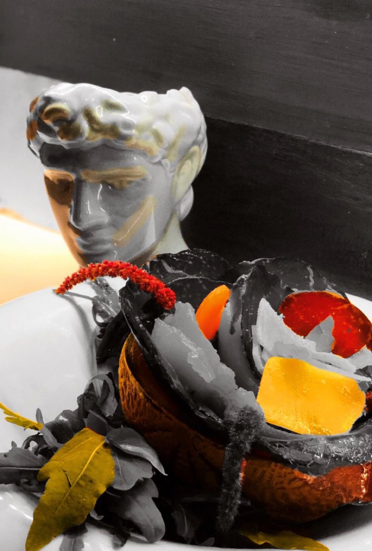 A classical sculpted head behind a decorative arrangement with red and yellow accents