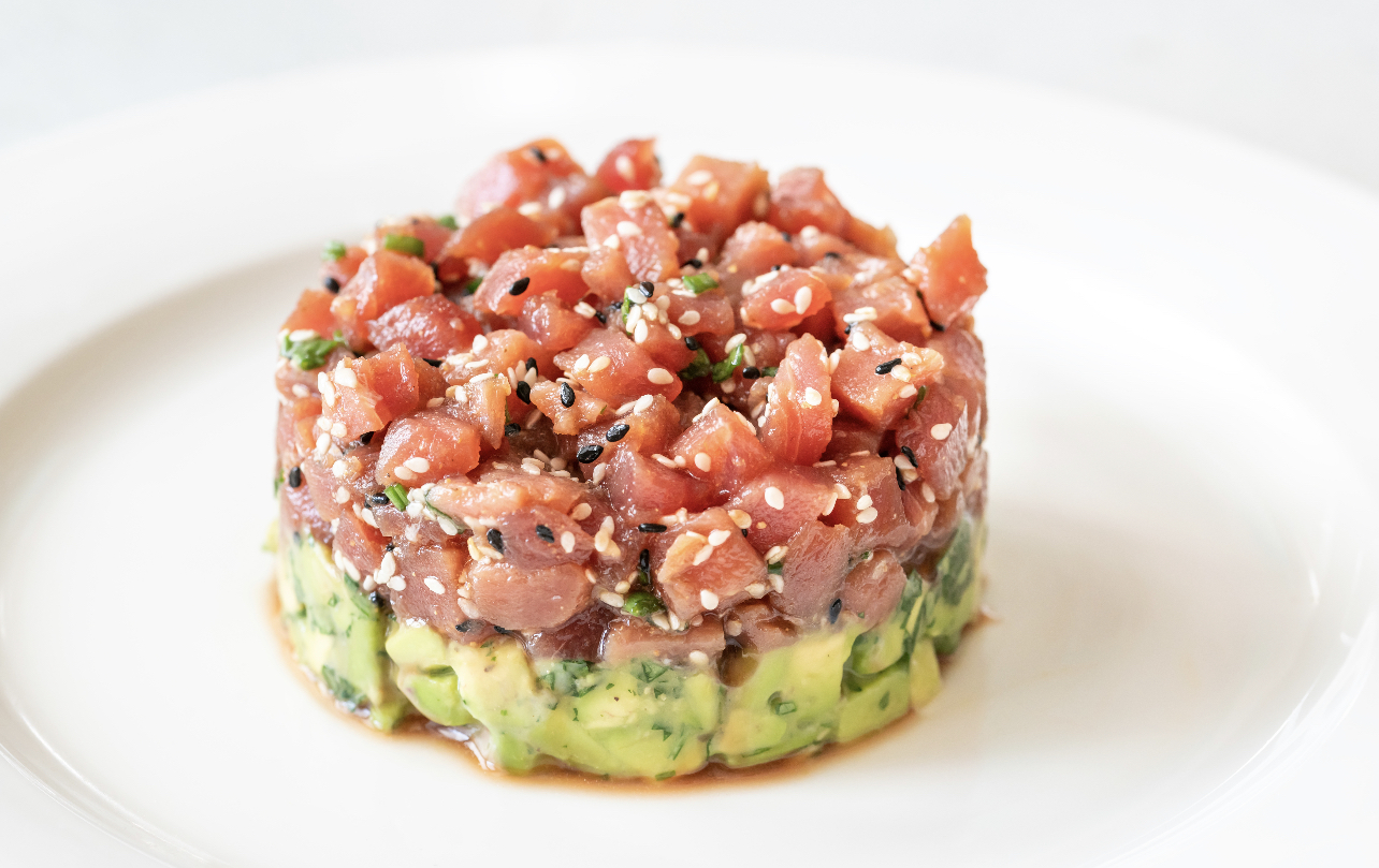 A round tartare over diced avocado, sprinkled with sesame seeds