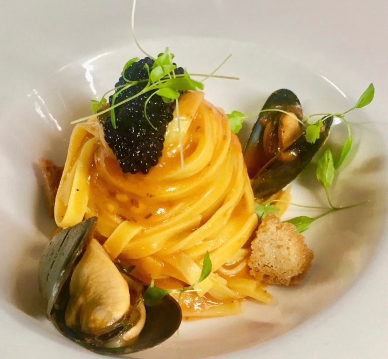 A nest of pasta with mussels, dark roe, croutons and small green leaves
