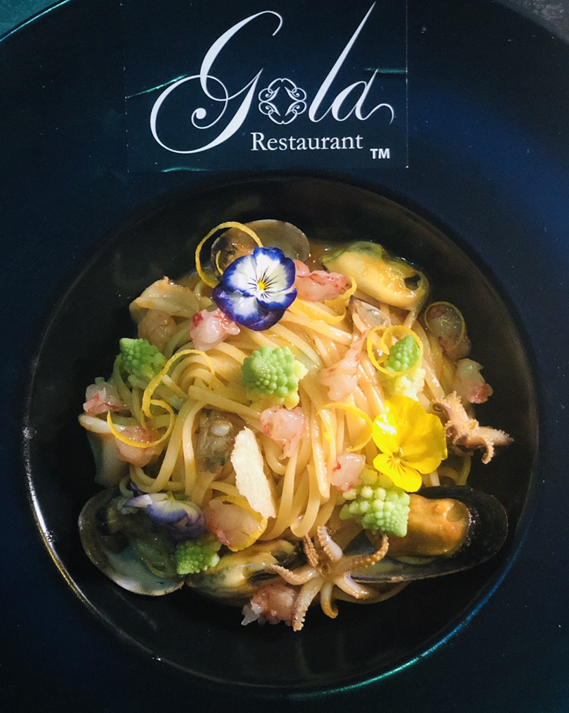 Ribbon pasta with seafood, lemon peel and flowers on a black plate